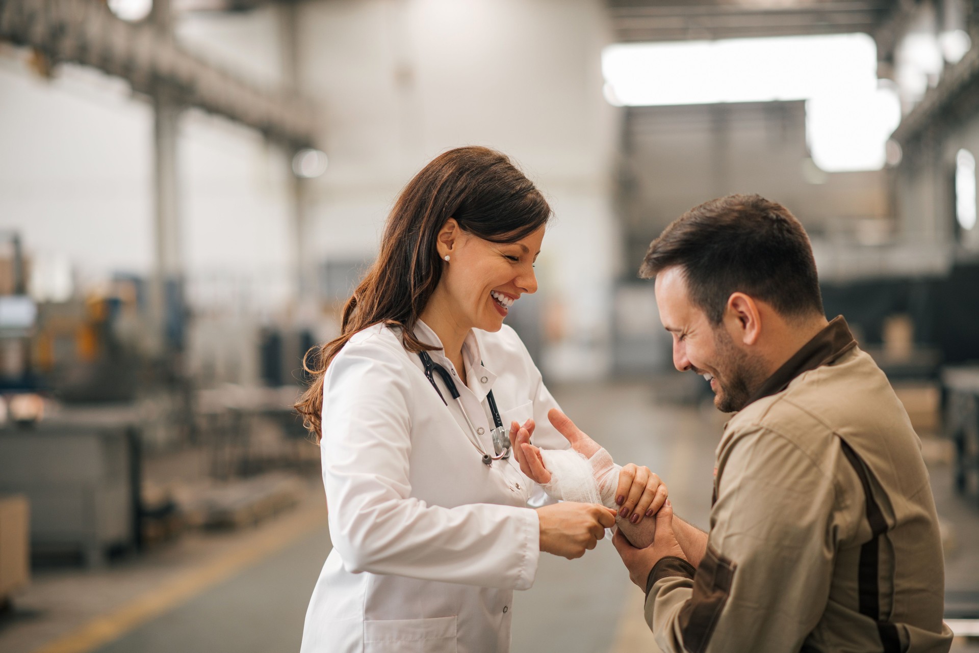 Smiling female doctor with injured worker in the industrial building.